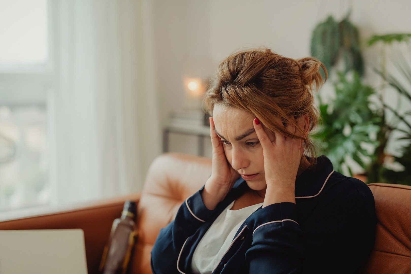 Stressed female caregiver sitting on couch with hands on head, overwhelmed and exhausted